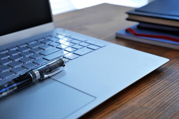 fountain pen on computer keyboard on wooden table with paper notebooks in the background - selective focus concept photo