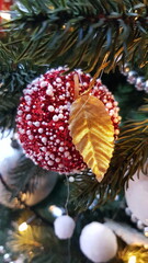Traditional Christmas bauble hanging on fir tree branches. Holiday decoration in shape of red apple covered with white artificial snow with golden leaf closeup