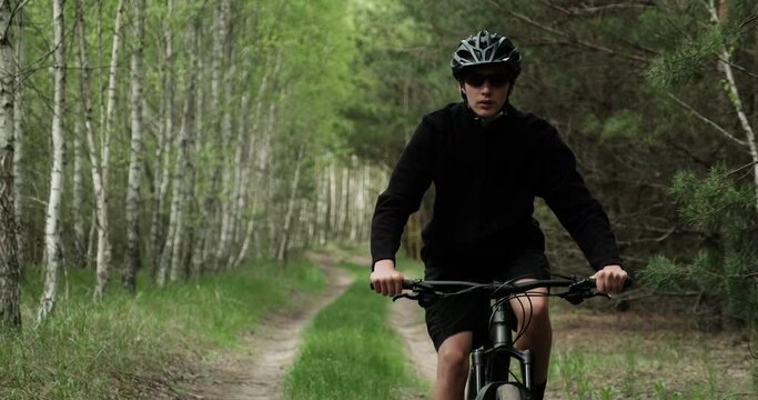 Young  man cyclist rides on a forest road. Teenager on a mountain bike rides through the forest. Man in a Bicycle helmet rides an mtb bike.