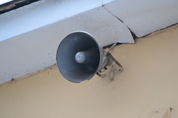 A closeup of a vintage gray loudspeaker hanging from a concrete wall.