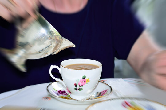 Elderly lady holding chrome milk jug over vintage bone china cup. Focal zoom effect. Concept of Mother's Day. Concept of aging and elderly care