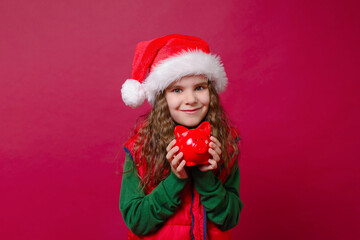 Cute girl kid holding a red piggy Bank or boar on a red background. Holidays, savings, traditions concept.