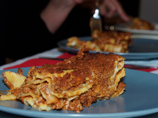 Dinner time at home with friends and family. A typical first course of Italian cuisine, lasagna, made with minced meat and tomato sauce.