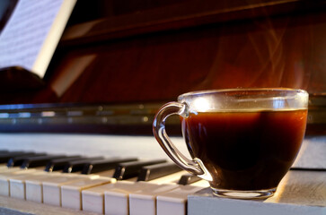 Closeup a Cup of Hot Coffee with Smoke on the Piano with Blurry Music Sheet