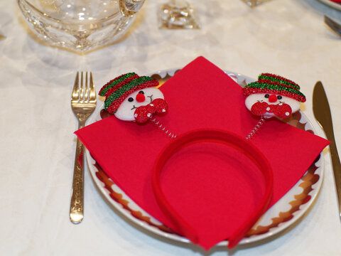 Decorations for a table set for Christmas dinner. A hair border featuring two snowmen resting on a plate waiting to be worn.