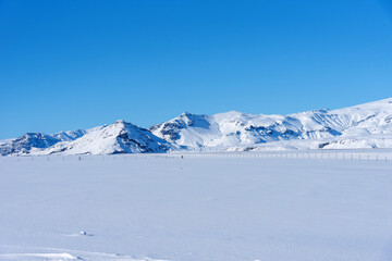 Fototapeta na wymiar Typical Icelandic winter landscape with mountains under the snow and blue sky. Beautiful winter landscape with mountains covered snow, cold frosty weather and white field in Iceland.
