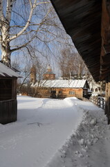 Snow-covered path, wooden houses, stone churches and a birch in a winter landscape.