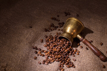 Coffee beans are scattered on a rough cloth. The coffee maker is lying next to coffee beans.
