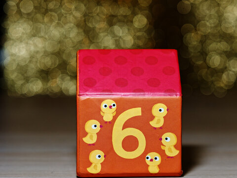 Children's toys around the house. A small numbered paper house with the design of six chicks on a gold background.