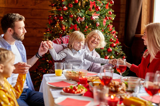 Family Holding Hands And Praying Before Christmas Holiday Dinner At Home, Christmas, New Year, Thanksgiving, Anniversary, Hanukkah, Easter Celebration Concept