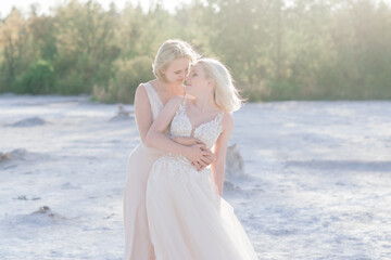 Fototapeta na wymiar Beautiful lesbian couple walking on sand along river bank on their wedding day
