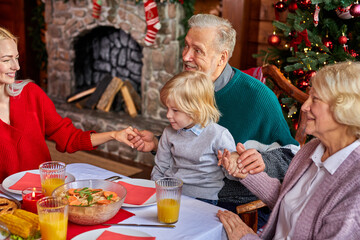 family having christmas dinner and praying before meal, multi-generation family enjoy celebrating new year with loved ones