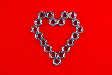 Heart made of metal nuts on a red background. Heart symbol for valentine's day. Love, romance, creativity