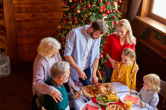 male is carving chicken for christmas or new year, children in anticipation of holiday, having pre-holiday mood - Powered by Adobe