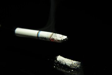 Lit cigarette with ash on a black background close-up, space for text, macro photography