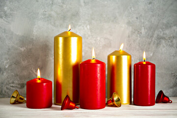 Bunch of red and golden candles burning on wood textured table with traditional decorative Christmas bells, grunged concrete wall background with a lot of copy space for text.
