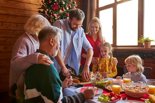 Family Celebrating Christmas At Home, Gathered Around The Table, Multi-generation. Having Christmas Dinner, Enjoying Winter Holiday Season At Home