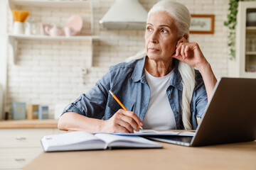 Pensive mature middle aged woman using laptop