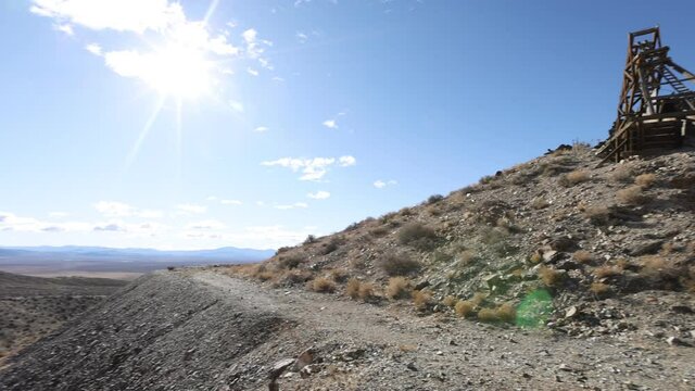 Pan right over dirt road in the desert past mining head frame and shaft built into hill
