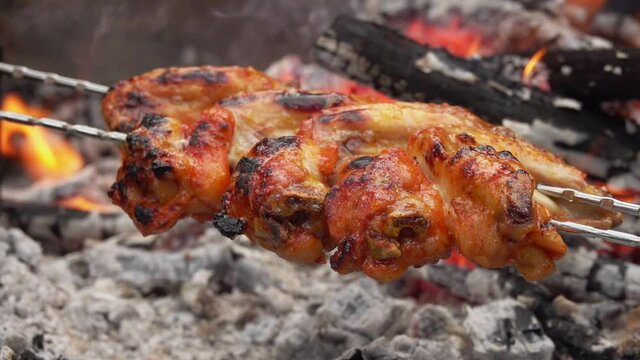 Delicious marinated chicken wings on the skewers are roasting above the open fire outdoors