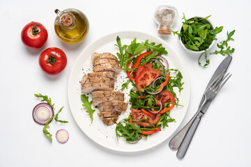 Baked chicken breast with vegetable salad. Chicken fillet with arugula, tomatoes and red bell pepper. White background, top view, copy space