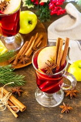 Winter Christmas hot drink with orange, apple and spices. Mulled wine in glass mug with spices on rustic table.