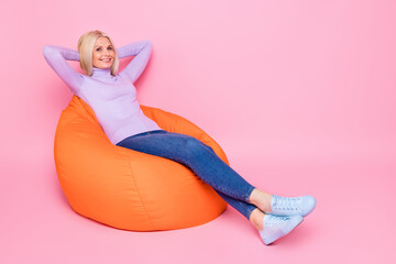 Full length body size photo of old woman laying relaxing in orange beanbag isolated on pastel pink color background
