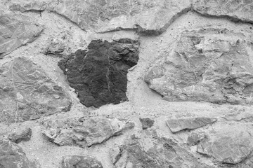 Wall of clay and large rough stones close-up in black and white frame colorless as background