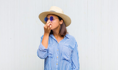 latin woman feeling disgusted, holding nose to avoid smelling a foul and unpleasant stench