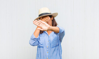 latin woman covering face with hand and putting other hand up front to stop camera, refusing photos...