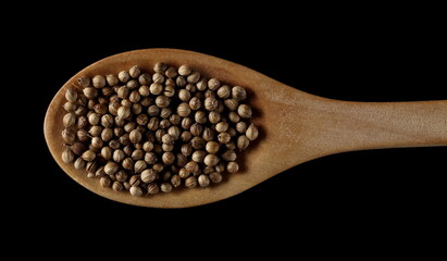 Coriander seeds with wooden spoon isolated on black background, top view