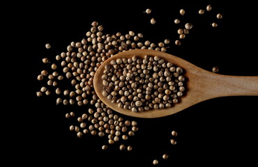 Coriander seeds with wooden spoon isolated on black background, top view