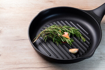 Black frying pan on a wooden board with rosemary sprigs and cloves of garlic inside