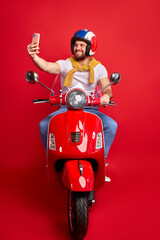 handsome biker man is taking photo while driving, caucasian guy in helmet make selfie on smartphone, isolated on red background