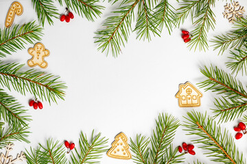 Christmas frame made of fir branches, red berries, gingerbread house on a white background. A Green Christmas concept. Merry christmas greeting card with empty space for holiday text.