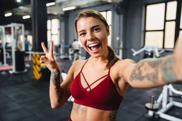 Fototapeta na wymiar Smiling sportswoman gesturing peace sign while taking selfie photo