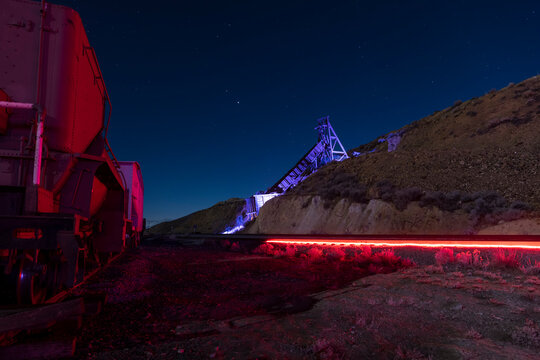 Lit up train tracks and train cars with a multicolored mining head frame in the desert