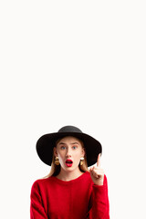 Omg face. Sale discount. Fashion look. Personal offer. Information banner. Shocked woman in red sweater black hat pointing up on copy space isolated on white.