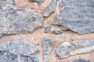Wall of large gray marble stones and pink clay close up as background