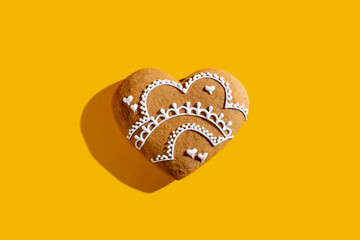 Festive biscuit. Valentine Day. Holiday bakery food. Beige homemade gingerbread heart cookie with white icing decoration isolated on bright orange background.