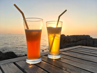 Frozen cocktail glasses with straws on wooden table over sea sunset