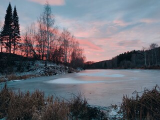 frozen pond near the forest against the background of a crimson sunset in the evening landscape