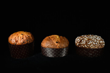 three types of Italian panettone: high, low and with almonds on a black background and with cutting light