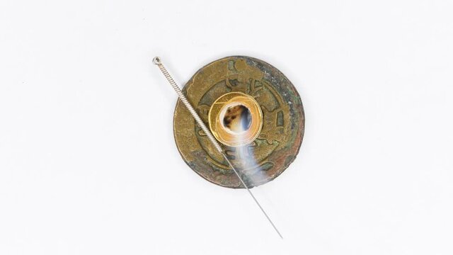 acupuncture needle and smoking moxibustion cone on antique Chinese coin