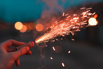 Young Man Lighting Up Firecracker in his Hand Outdoors in Evening. Guy Getting Ready for New Year Fun with Fireworks or Pyrotechnic Products - CloseUp Shot - obrazy, fototapety, plakaty