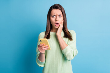 Photo portrait of worried woman touching face cheek with one hand holding yellow phone isolated on pastel blue colored background