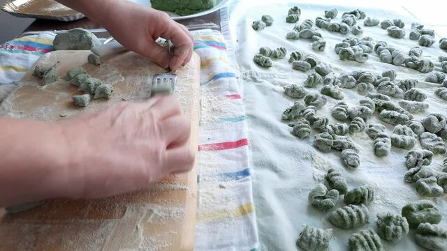 Real time video of female hands making raw spinach and potato gnocchi. Fresch green homemade italian dough dumplings on a towel.