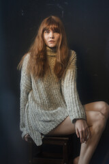 redhead woman in a knitted sweater sits on a chair