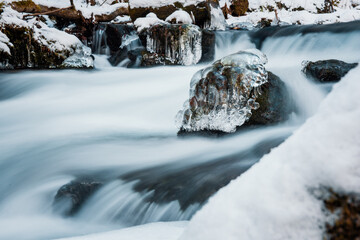 Flow of the river in frozen landscape. Frozen rocks in frozen river.