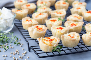 Mini quiche muffins with feta cheese, fried onion, thyme and red bell pepper, on a cooling rack, horizontal